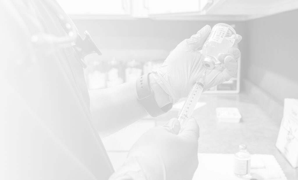 Dr Agarwals wearing blue disposable gloves is using a syringe to draw clear liquid from a small glass vial. The professional is wearing dark scrubs and a stethoscope is visible around their neck. The vial is labeled, though the text is partially obscured with a white overlay.